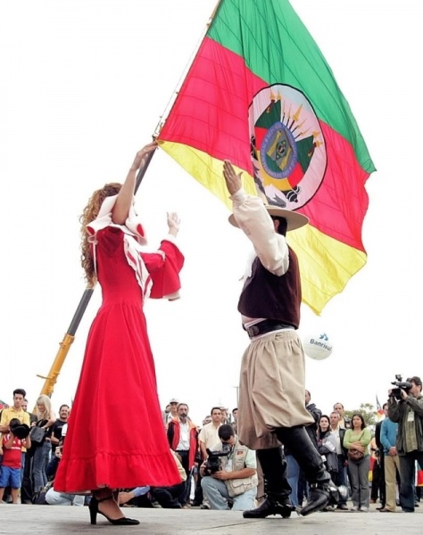 Arquivo:O Peão e a Prenda dançando com a bandeira do Estado do Rio Grande do Sul ao fundo.jpg